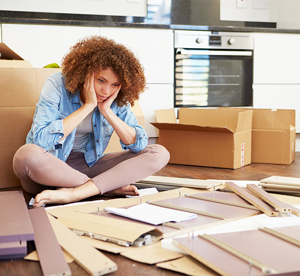 woman looking frustrated next to a pile of disassembled furniture