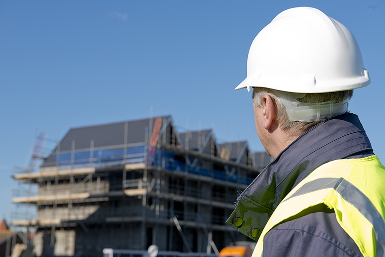 Coronavirus: Man in hard hat looking at unfinished apartment block