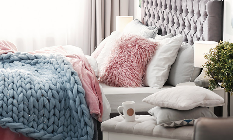Grey fabric bed with lots of cushions and blankets