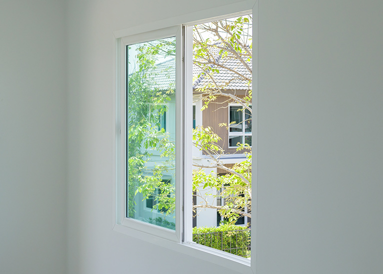 Slider window in house, looking out onto sunlit trees.