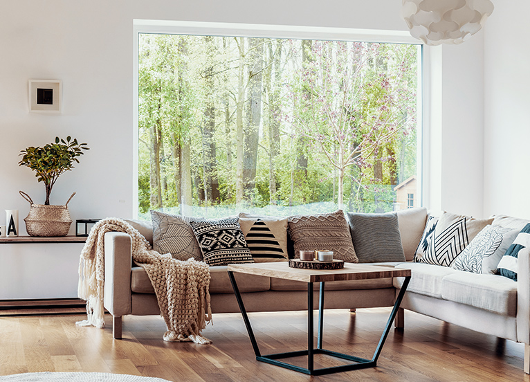 Large picture window, set back behind a couch in a modern home. Window shows wide view of forest trees.