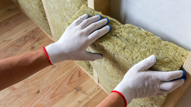 Close-up of worker hands in white gloves inserting rock wool insulation in wooden frame.