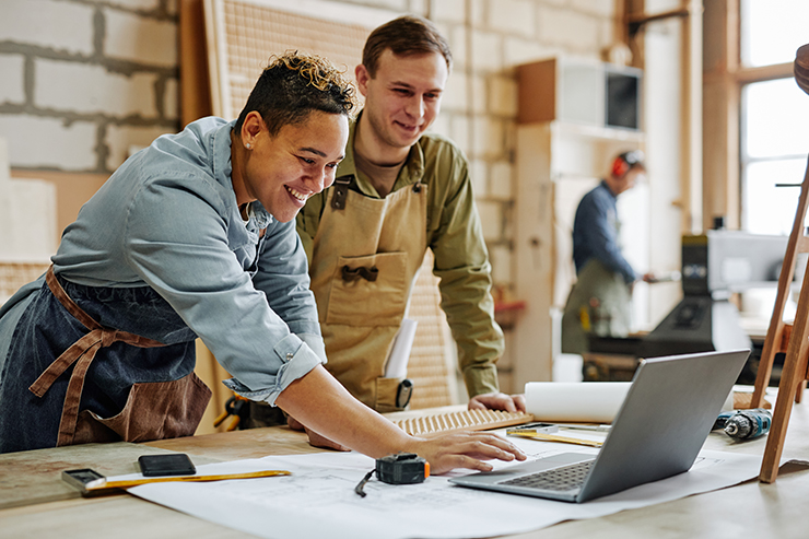 Photo of happy tradespeople checking blueprints on a laptop in a workshop