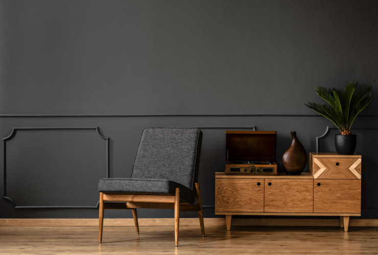 Picture of a black wooden chair next to a wooden cabinet with black painted walls and wooden floors