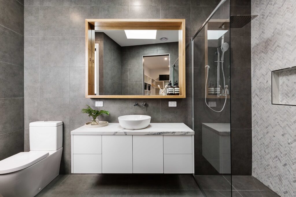 Picture of a modern bathroom with grey marble walls, a walk in shower and a large square mirror