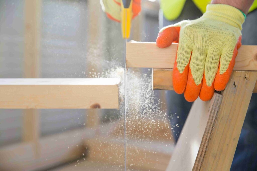 Picture of a builder sawing into a piece of wood wearing protective yellow and orange work gloves