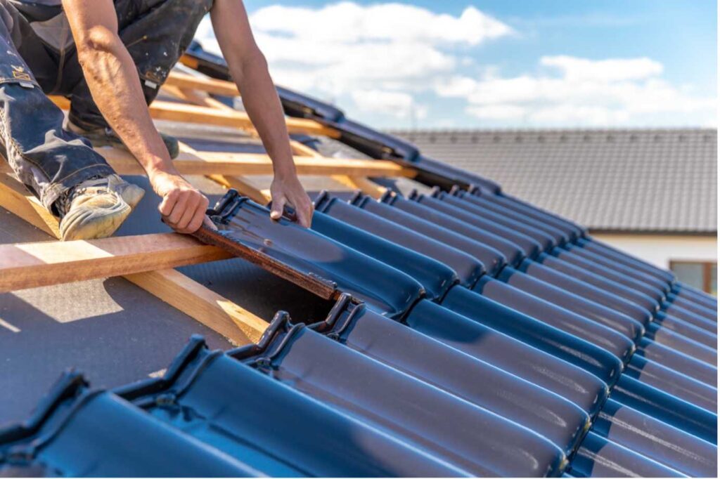  Picture of a roof specialist sitting on a roof installing roof tiles on a wooden frame
