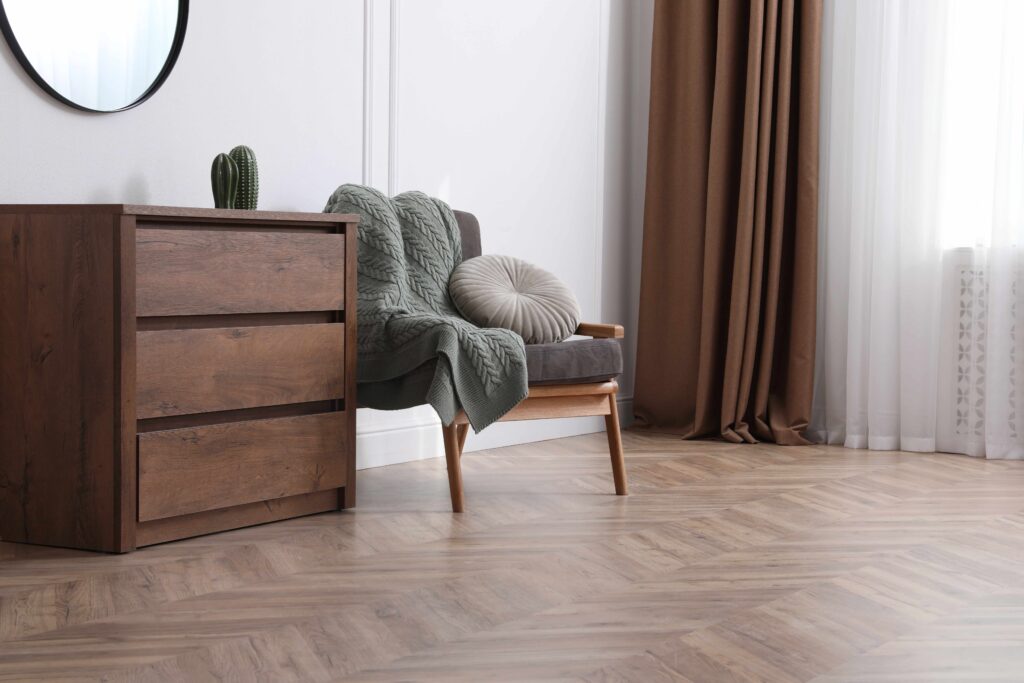 Picture of a wooden floor in living room with brown curtains and a brown chest of drawers beside a chair