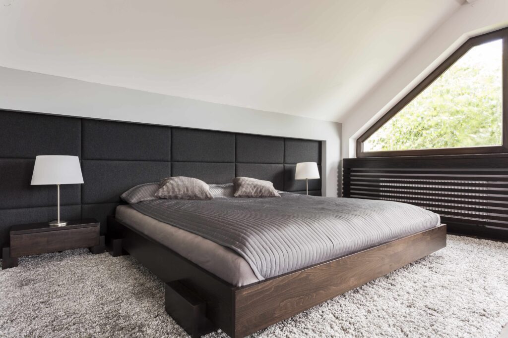 Picture of a modern bedroom with grey carpet and bedding, black panels on the back wall and a wooden bedframe