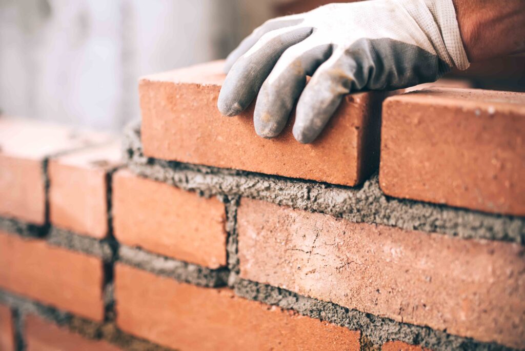 Picture of a bricklayer’s gloved hand applying mortar to set a brick into place on a brick wall