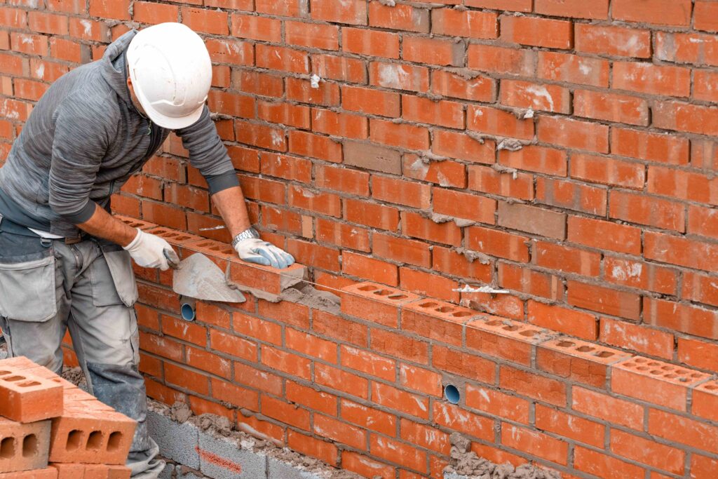 Picture of a bricklayer applying mortar to a brick wall to set a brick into place] 