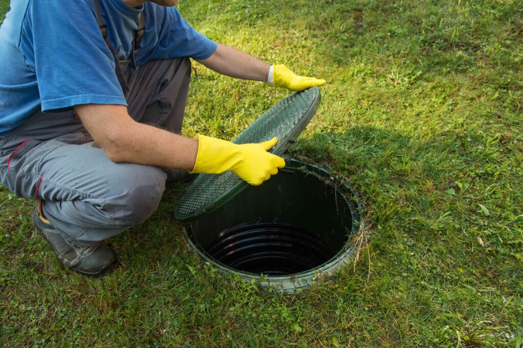 Picture of a drainage specialist removing lid from a septic underground tank
