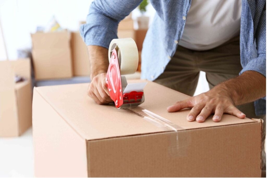 Picture of a man in a blue shirt taping a box shut during a house move