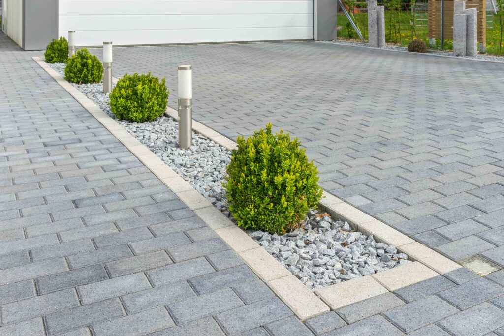 : Picture of a grey brick driveway with small shrubs on a gravel bed as decorative driveway dividers