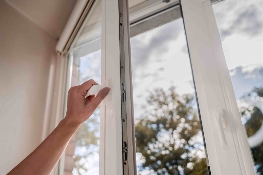 Picture of a hand opening a white framed window with a view of cloudy sky and trees