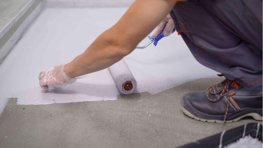 Picture of a tradesperson painting a floor with a paint roller wearing plastic gloves and boots