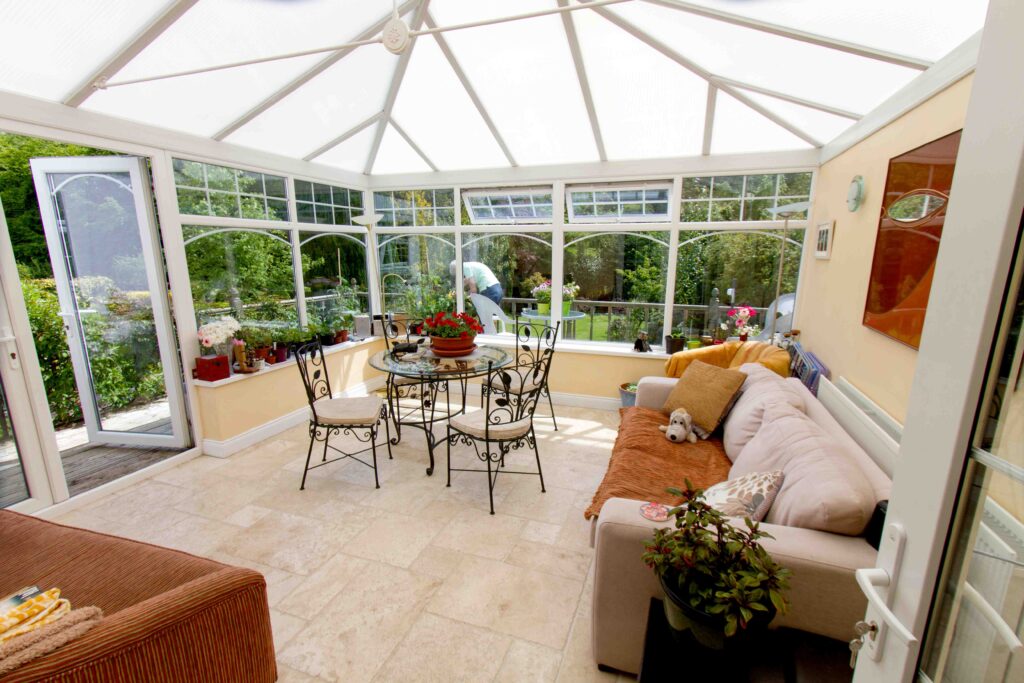 Picture of a patio with a sofa and small round table and chairs, with open doors leading to a garden