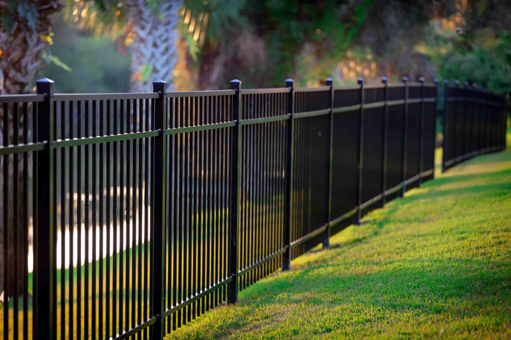 Picture of a metal fence painted black and installed on a bed of grass with trees in the background