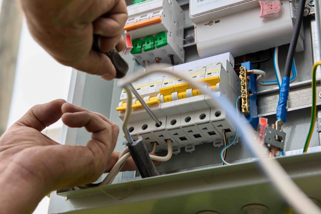 Picture of an electrician fastening a fuse board circuit breaker onto a consumer unit electrical panel