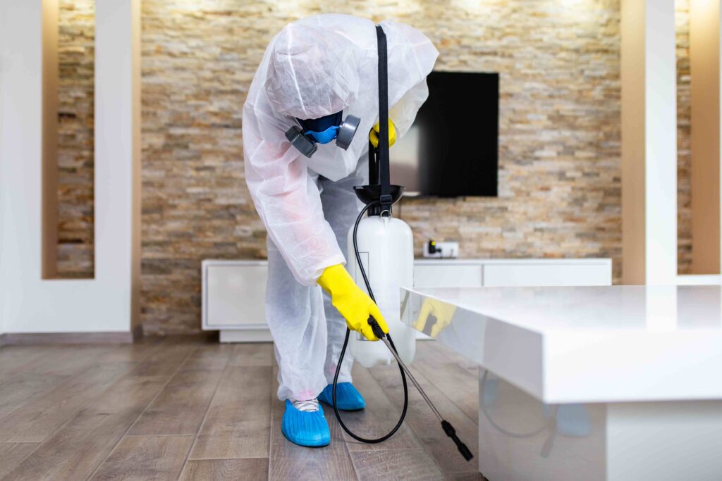 Picture of a pest control specialist fumigating a property wearing a protective suit and mask