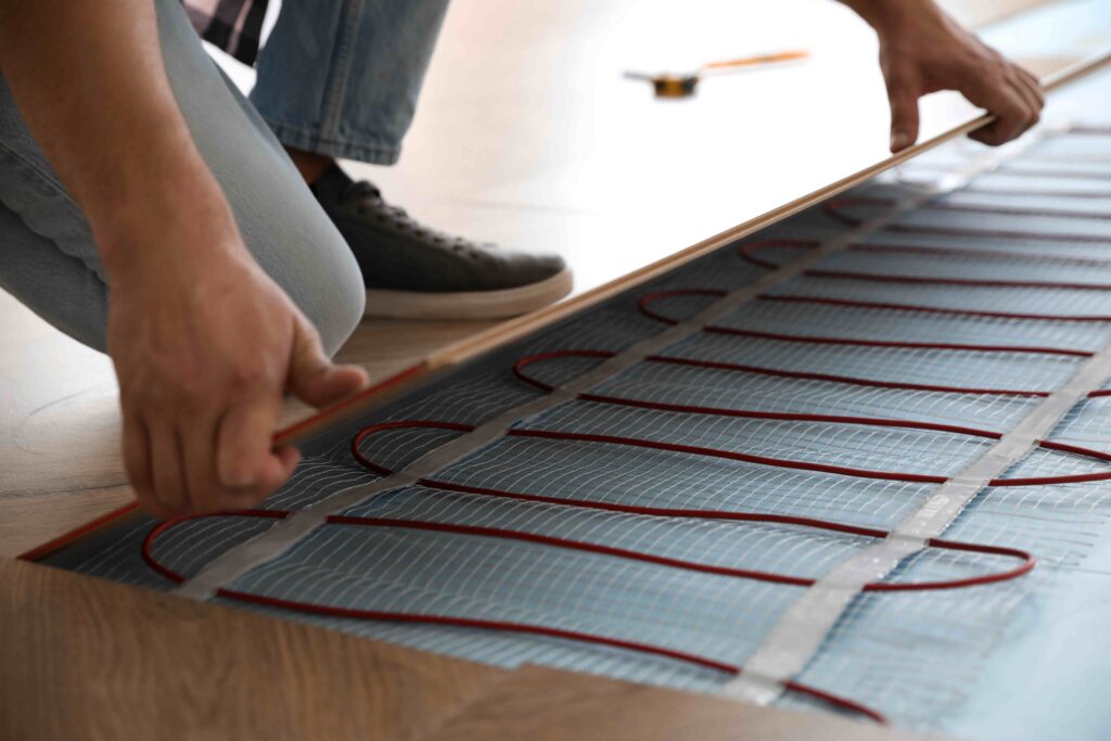 Picture of an electrician installing electric underfloor heating underneath wooden flooring